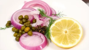 Finished towering NYC deli-style lox and cream cheese bagel topped with translucent paper-thin red onion slices, scattered briny capers, torn fresh dill sprigs, cracked black pepper, and a bright yellow lemon wedge being squeezed â ready for the first bite